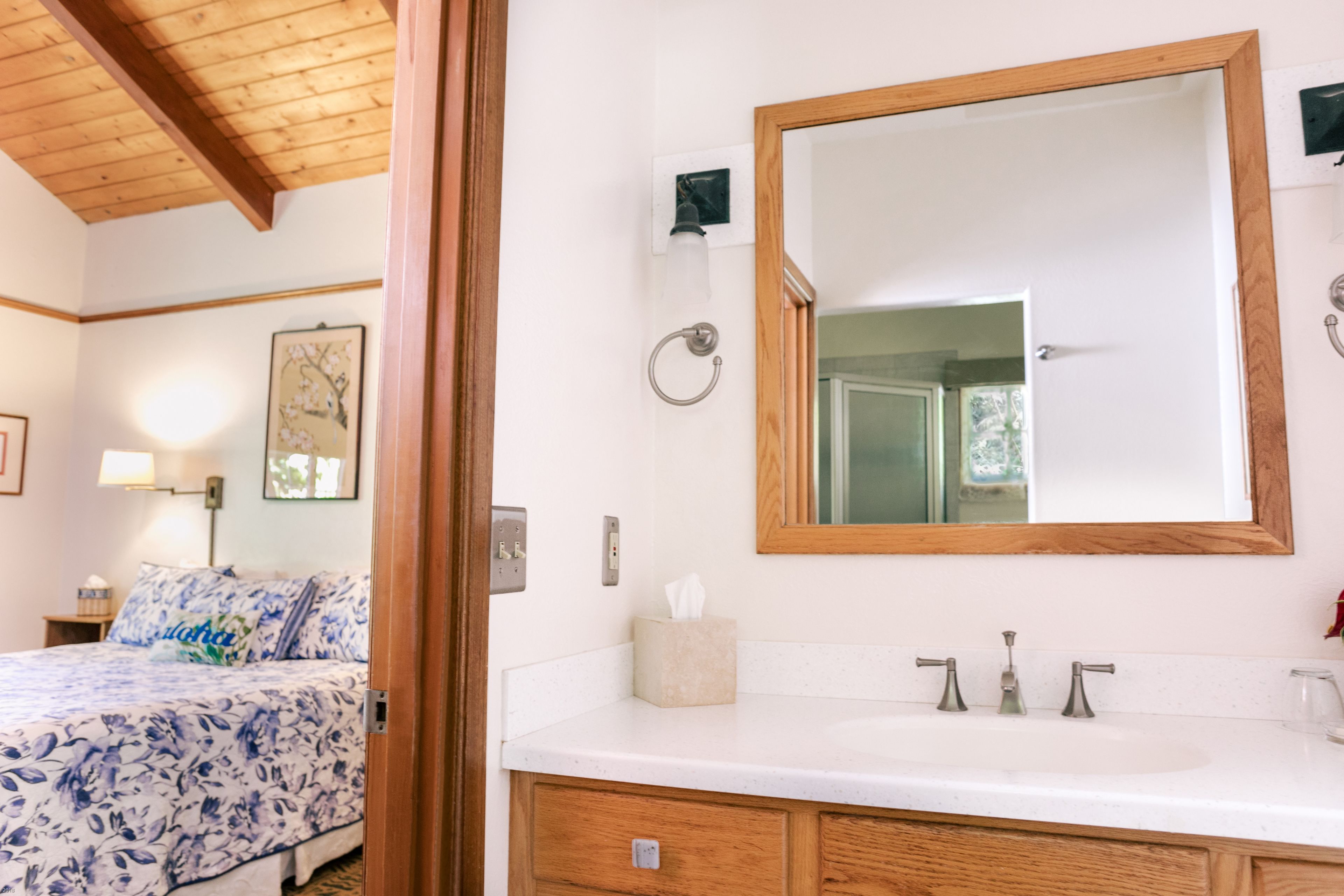 Un dormitorio con cama, mesita de noche con lámpara, espejo y baño con lavabo y espejo.