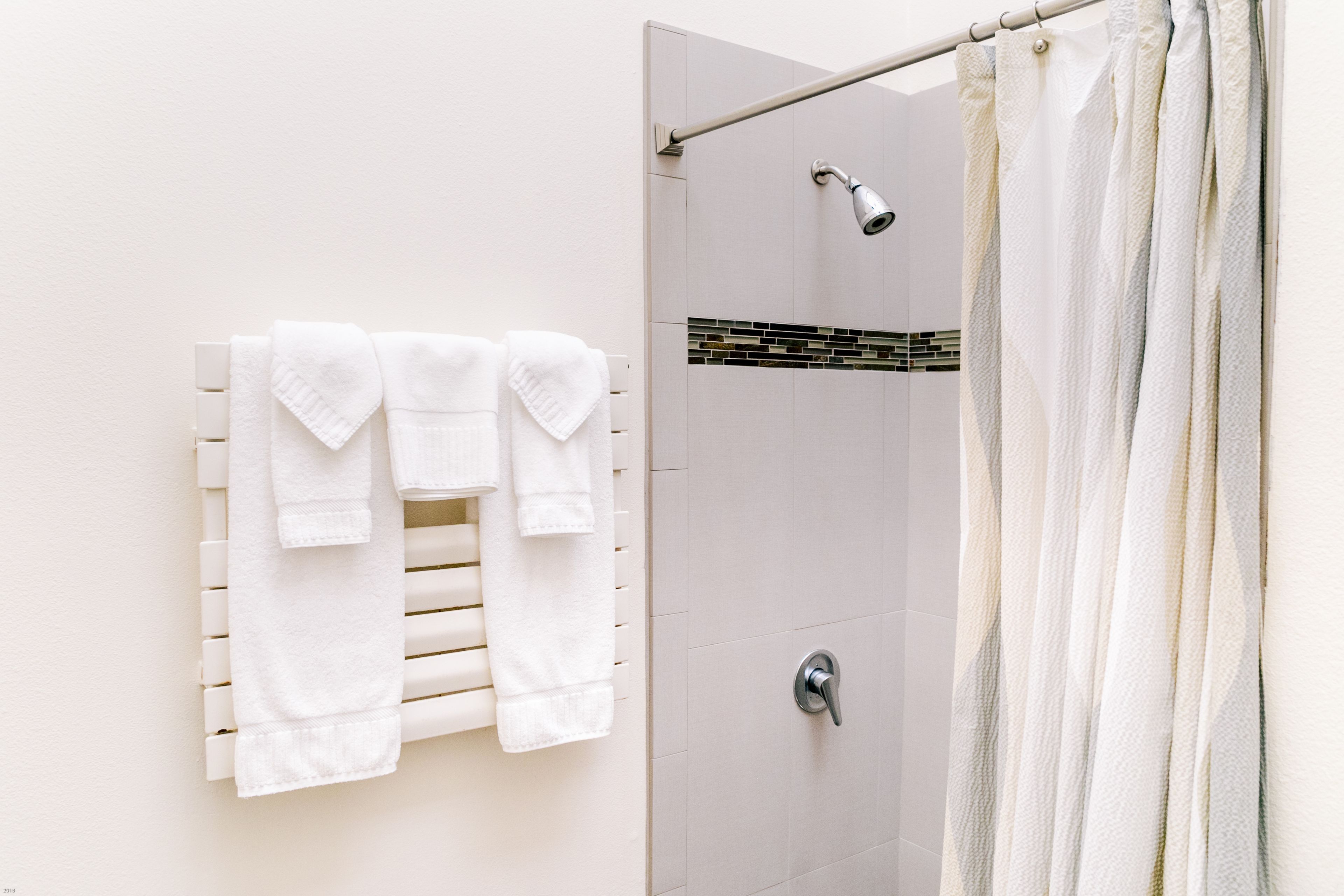 A shower area with a white tiled wall, a showerhead, and a towel rack with folded towels.