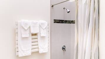 A shower area with a white tiled wall, a showerhead, and a towel rack with folded towels.