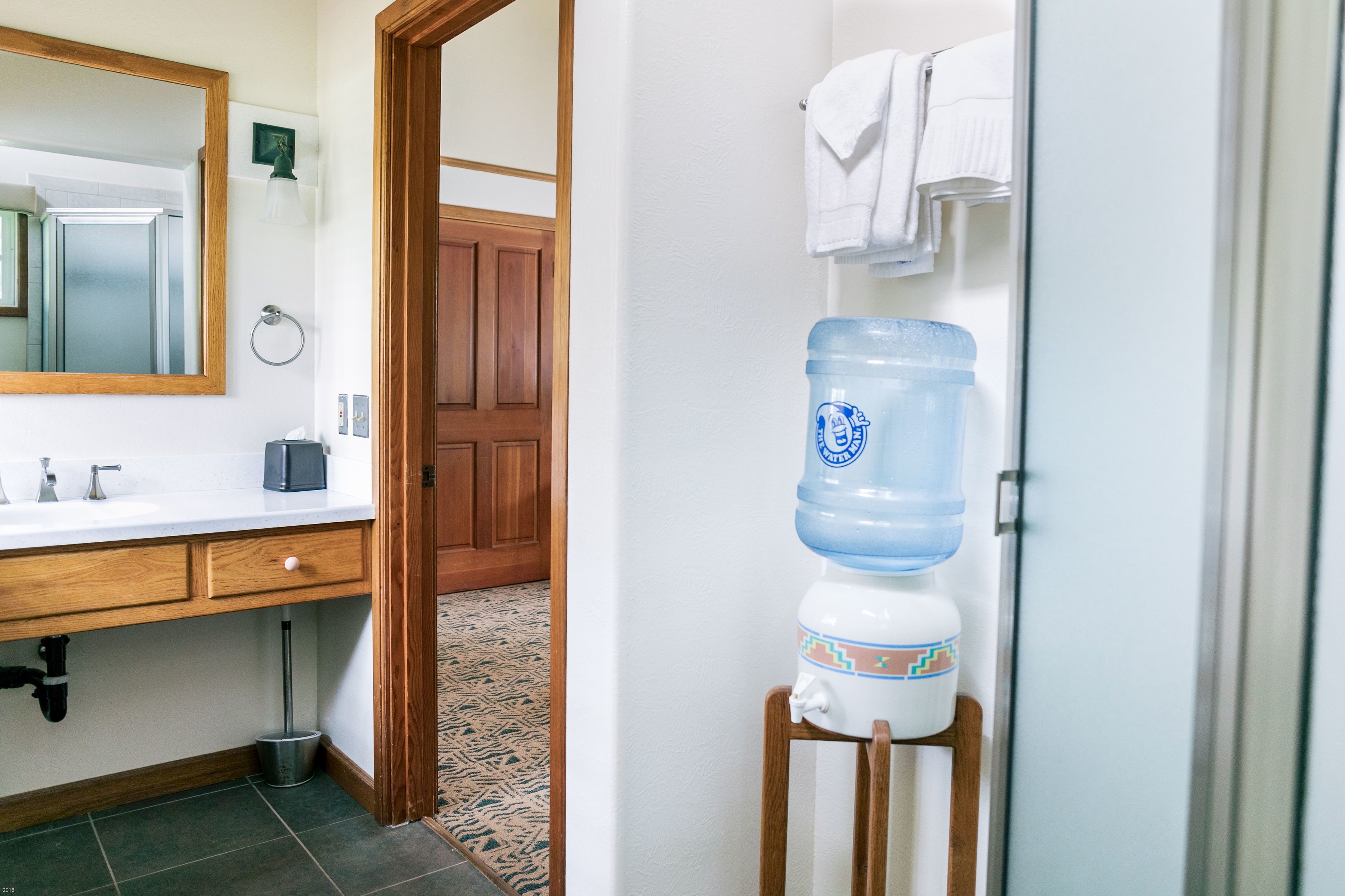 A bathroom with a large water dispenser, a wooden door, and a mirror.