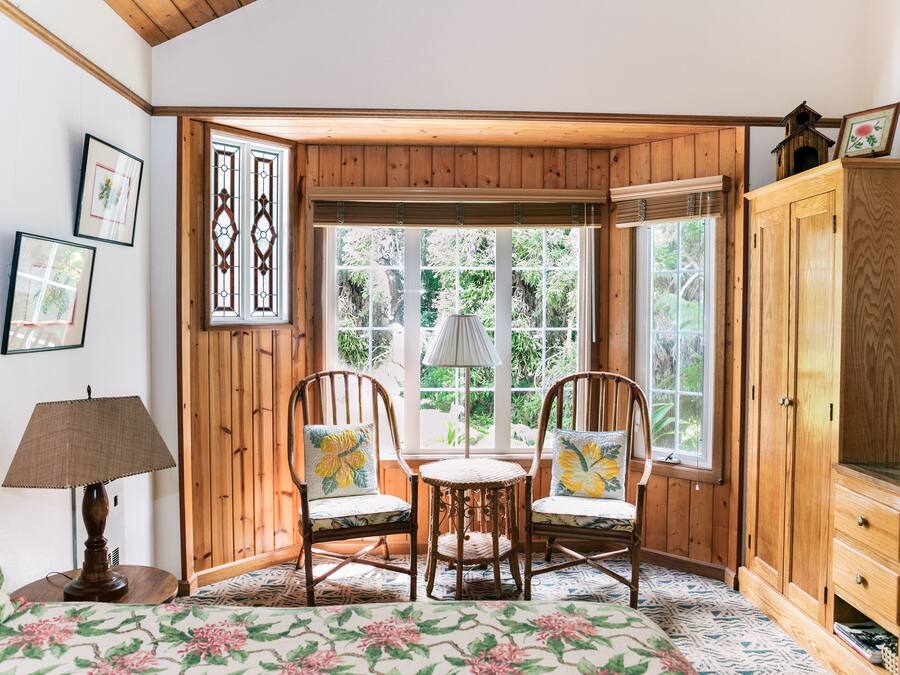 Un coin douillet avec deux fauteuils à bascule, une petite table et une lampe. Les murs sont ornés de tableaux encadrés et il y a une armoire en bois.