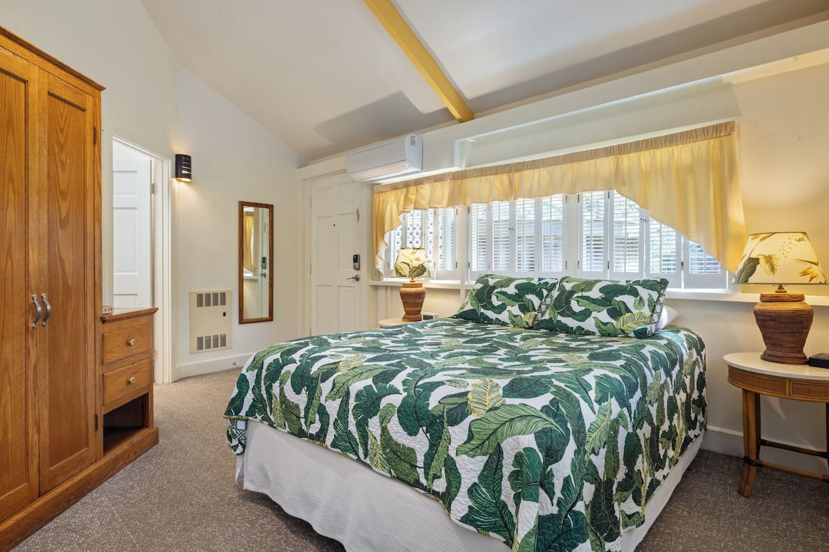 A bedroom with a large bed, a wooden wardrobe, a bedside table with a lamp, and a window with curtains.