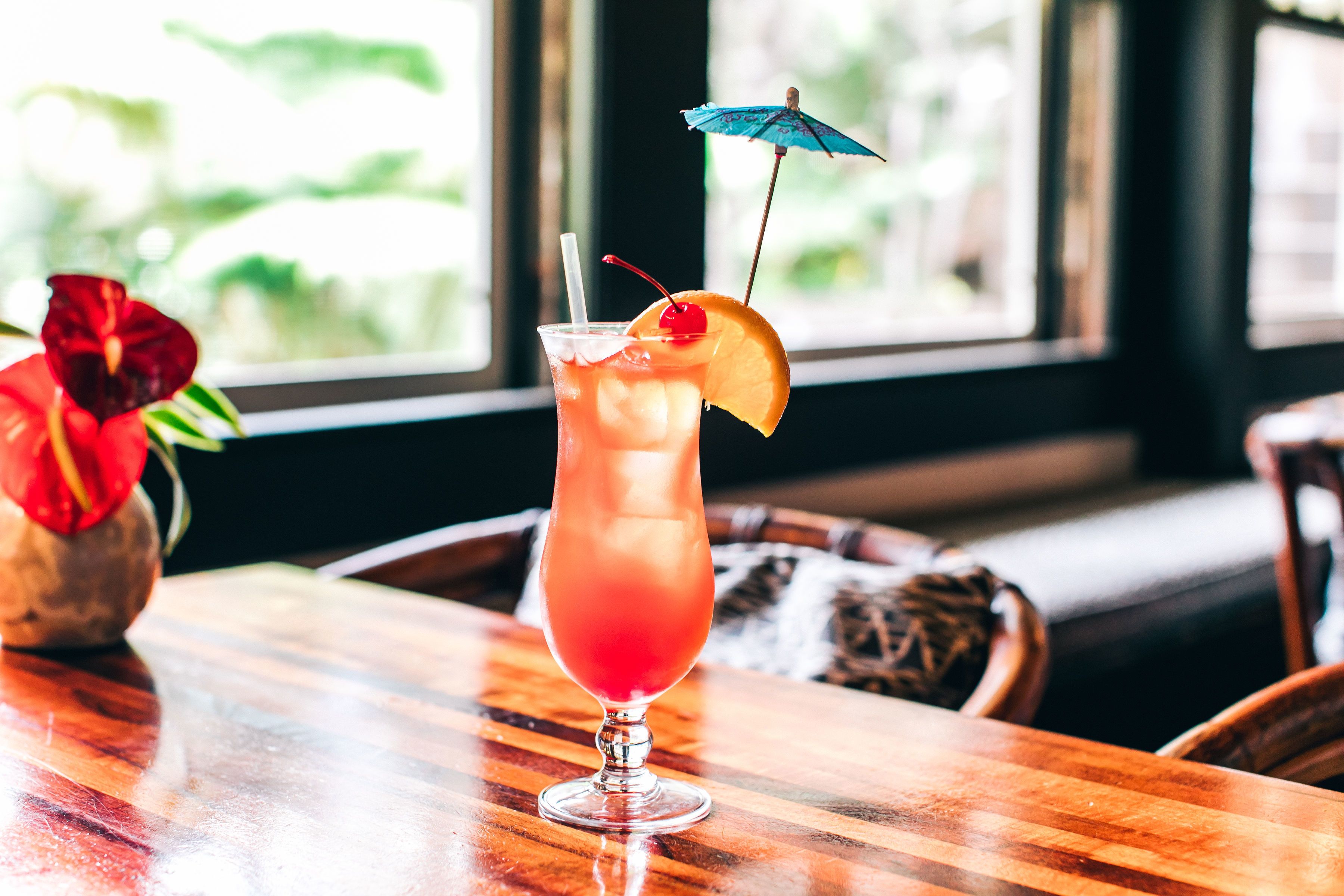 A cocktail glass with a straw, a cherry, and a slice of orange on a wooden table.
