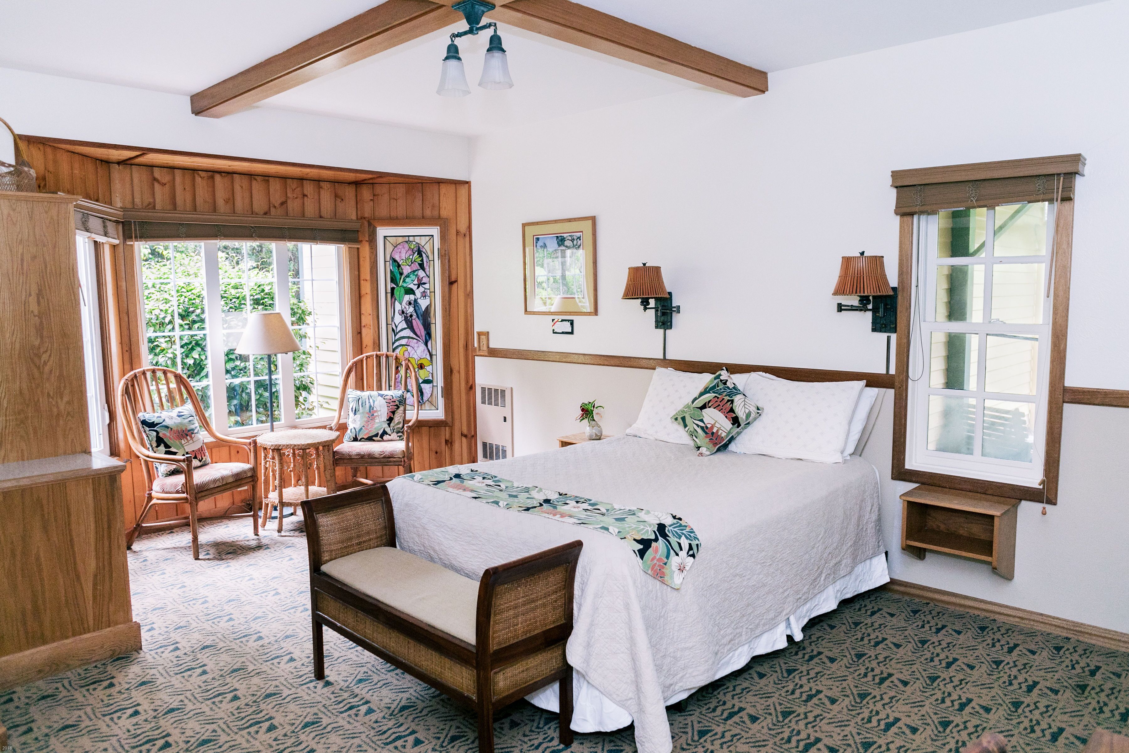 A bedroom with a bed, two chairs, a small table, a lamp, and a window.