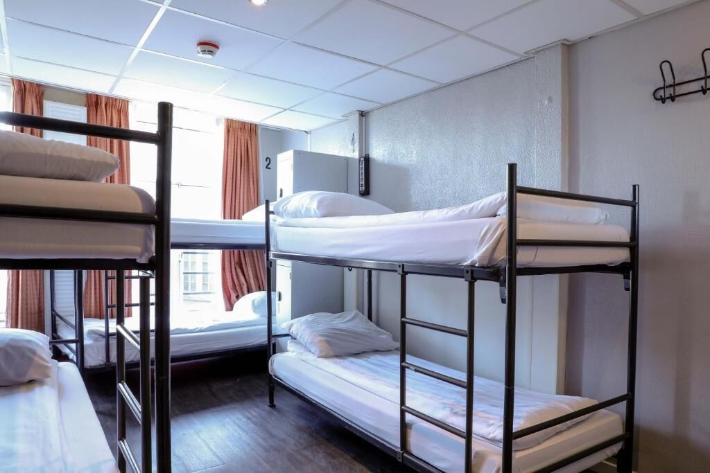 A dormitory room with bunk beds, a window with curtains, and a wall-mounted air conditioning unit.