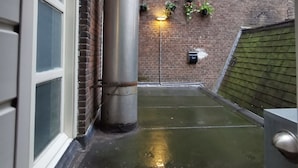 A narrow alleyway with a brick wall, a metal column, and a green awning.