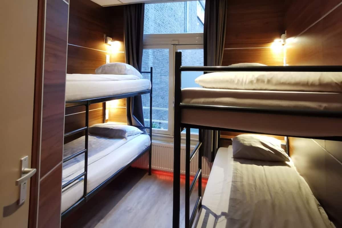 A dormitory room with bunk beds, a window with curtains, and a ceiling light.