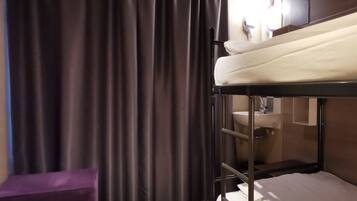 A bunk bed room with a window, curtains, a small purple ottoman, and a sink in the corner.