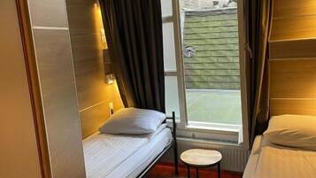 Une chambre d’hôtel de taille réduite, avec deux lits, une petite table ronde et une fenêtre avec des rideaux.