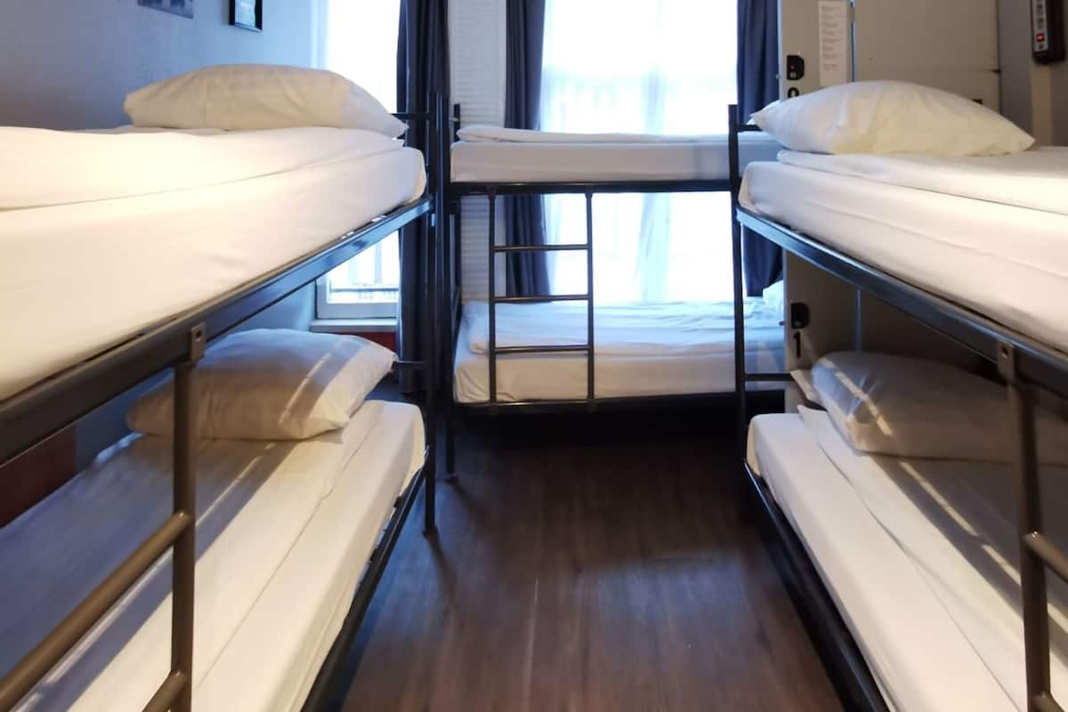A narrow, well-lit cabin with bunk beds, a window with curtains, and a wall-mounted phone.
