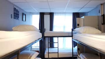 A narrow, well-lit cabin with bunk beds, a window with curtains, and a wall-mounted phone.