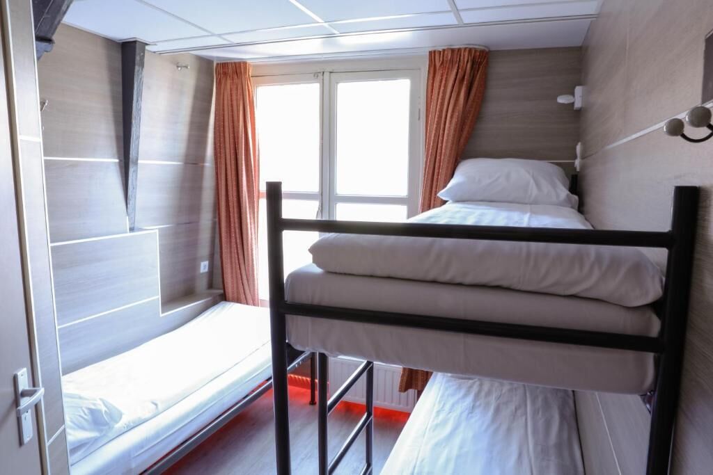 A bunk bed room with a window, curtains, and a bed with white bedding.