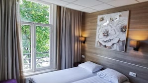 A hotel room with a large window, a bed with white linens, a wall-mounted artwork of flowers, and two bedside lamps.