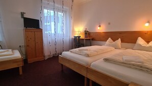 Habitación de hotel con dos camas, cabecero de madera, televisor sobre un mueble bajo, escritorio con lámpara y ventana con cortinas.