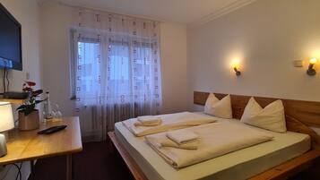 Quarto de hotel com cama, mesa de cabeceira, abajur e televisão fixada na parede.