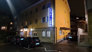 Un hotel con fachada amarilla, un letrero azul y varios coches aparcados adelante.