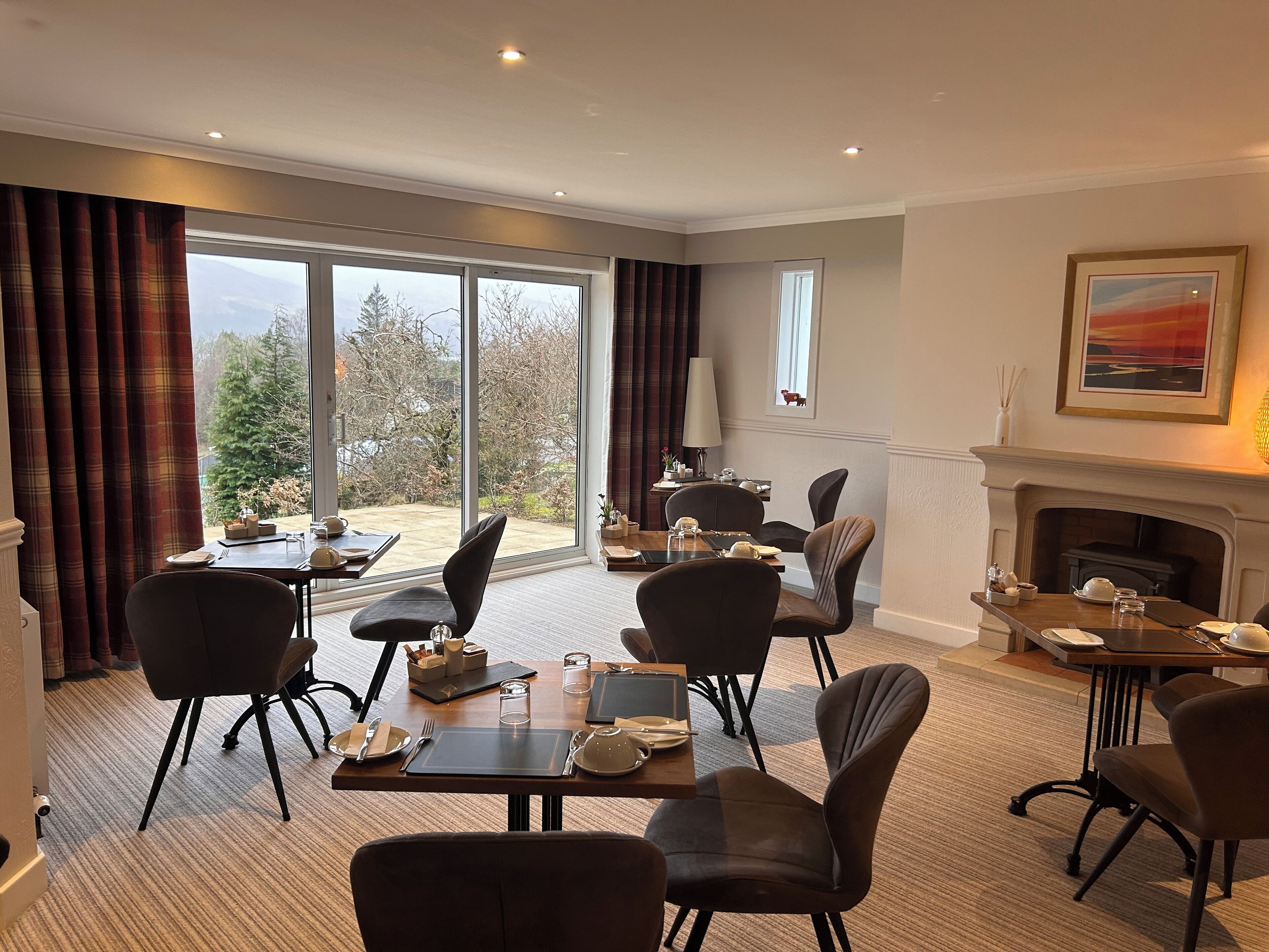 A dining area with a fireplace, large windows, and a view of trees.
