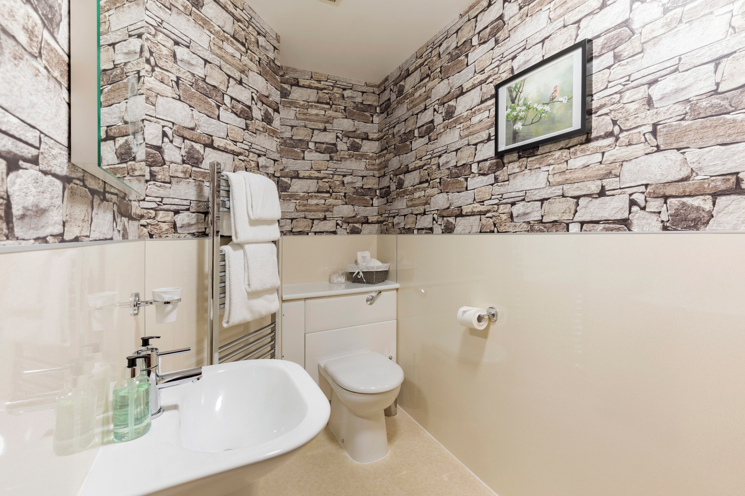 A bathroom with a stone wall, a sink, a toilet, and a framed picture on the wall.