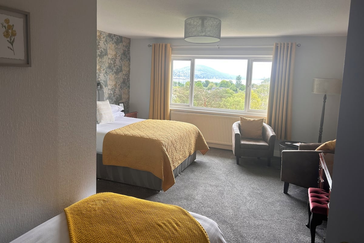 A hotel room with two beds, a view of the outdoors, a chair, and a desk.