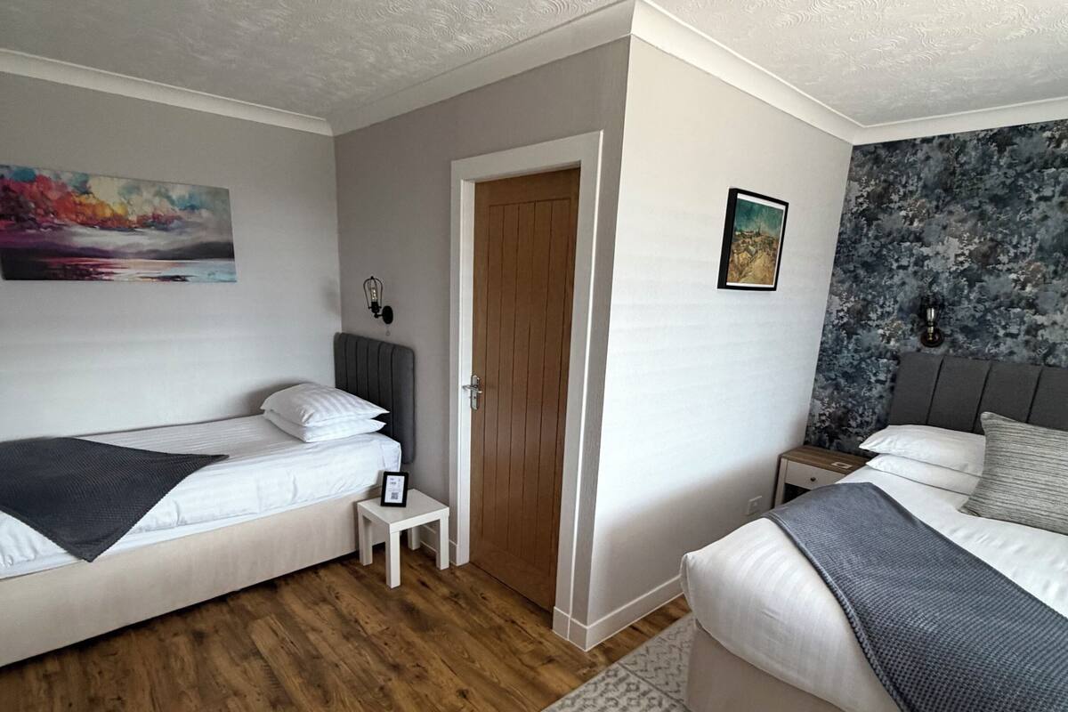 A bedroom with two beds, a wooden floor, a small bedside table, and a nightstand.
