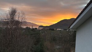 Ein Wohngebiet mit Blick auf einen Sonnenuntergang über Bergen, einem Rasen und einem weißen Gebäude mit einer gefliesten Terrasse.