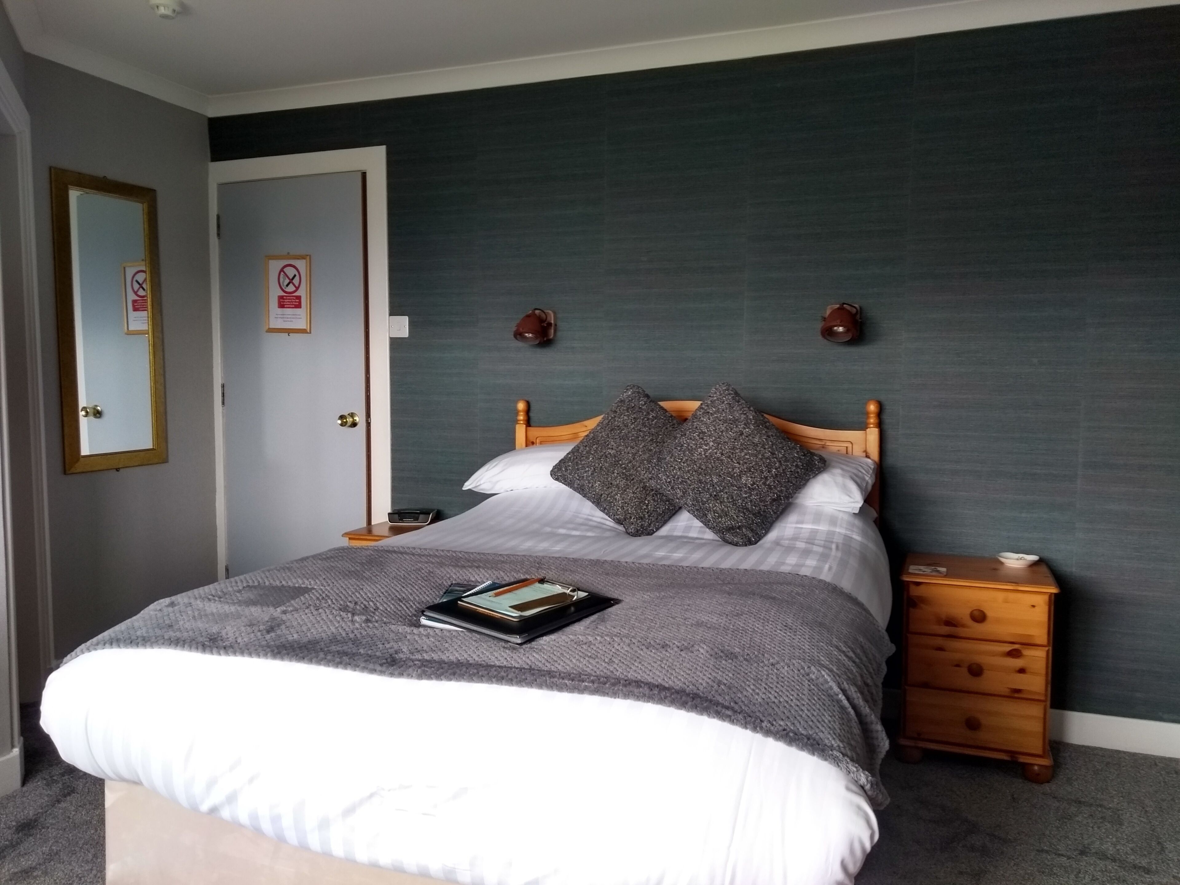 A neatly made bed with pillows, a bedside table with a book, and a wall-mounted clock.