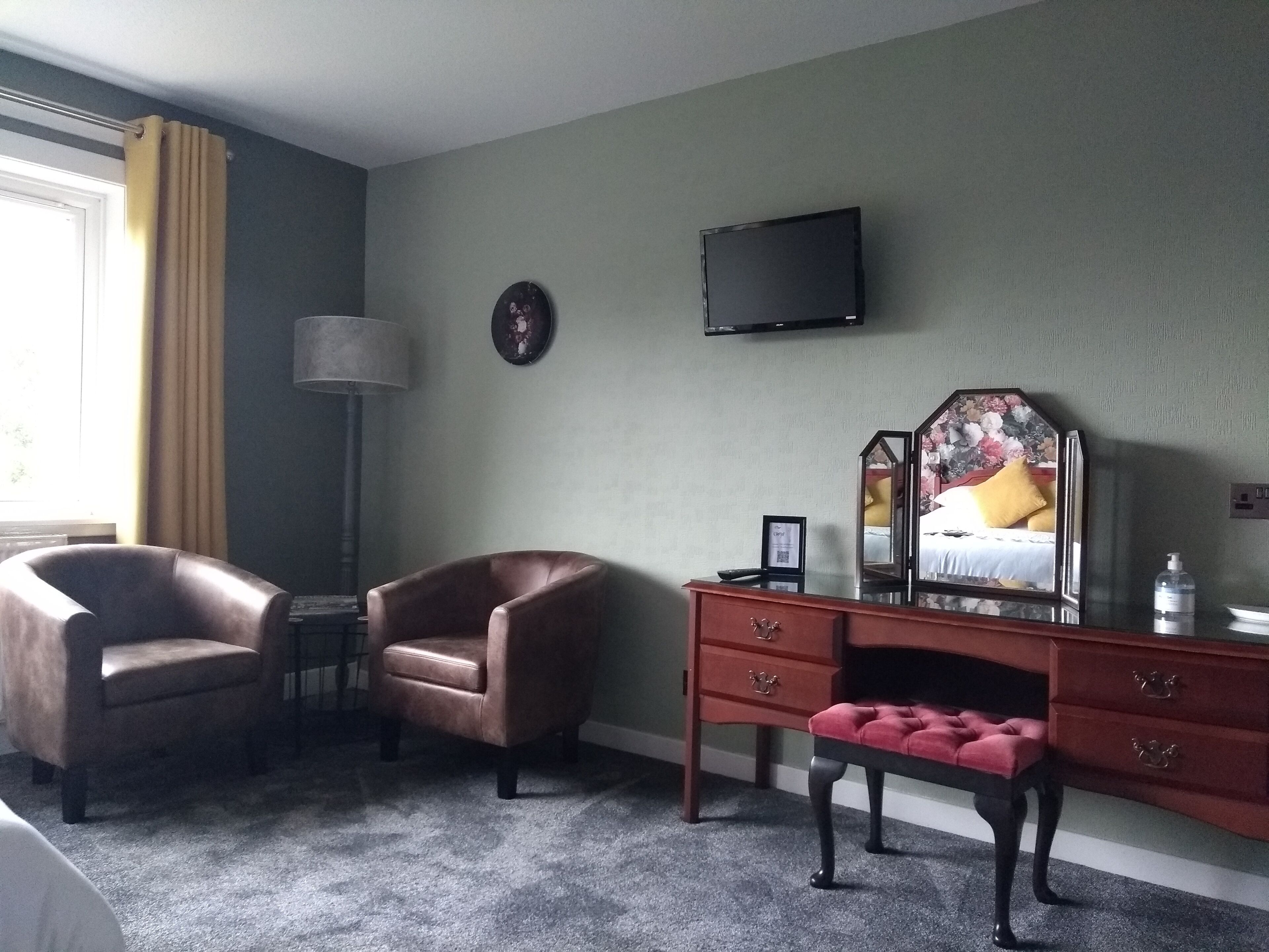 A hotel room with a brown leather chair, a wooden desk with drawers, a mirror, and a television mounted on the wall.