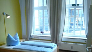Una camera d'albergo con due letti in legno, un termosifone e una finestra con tende.