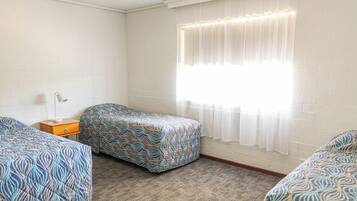 A room with two beds, a nightstand, and a window with sheer curtains.
