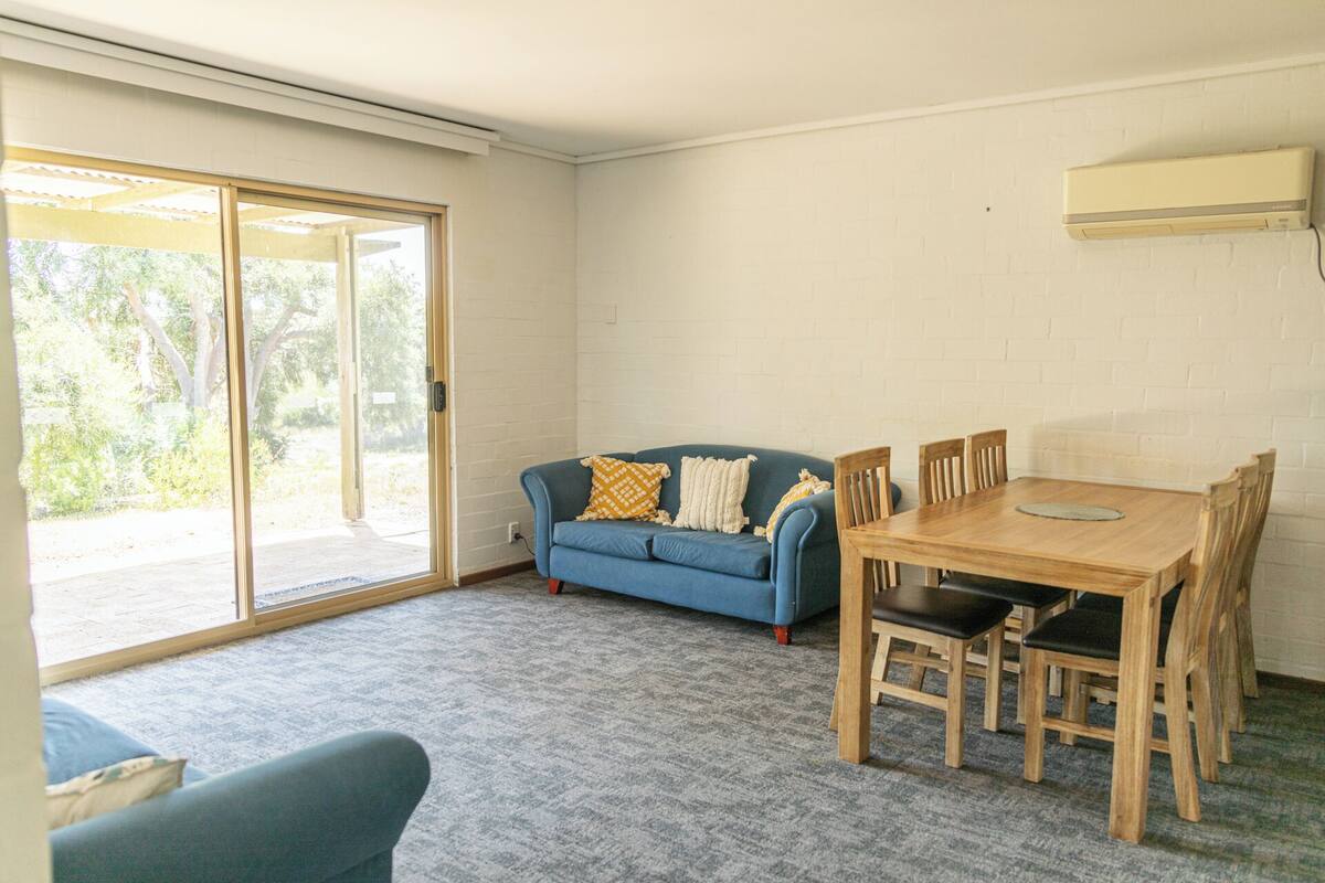 A room with a blue sofa, a wooden dining table with chairs, and a sliding glass door leading to an outdoor area.