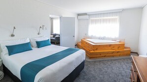 A hotel room with a large bed, a wooden bench with a bathtub, a desk, and a window with curtains.