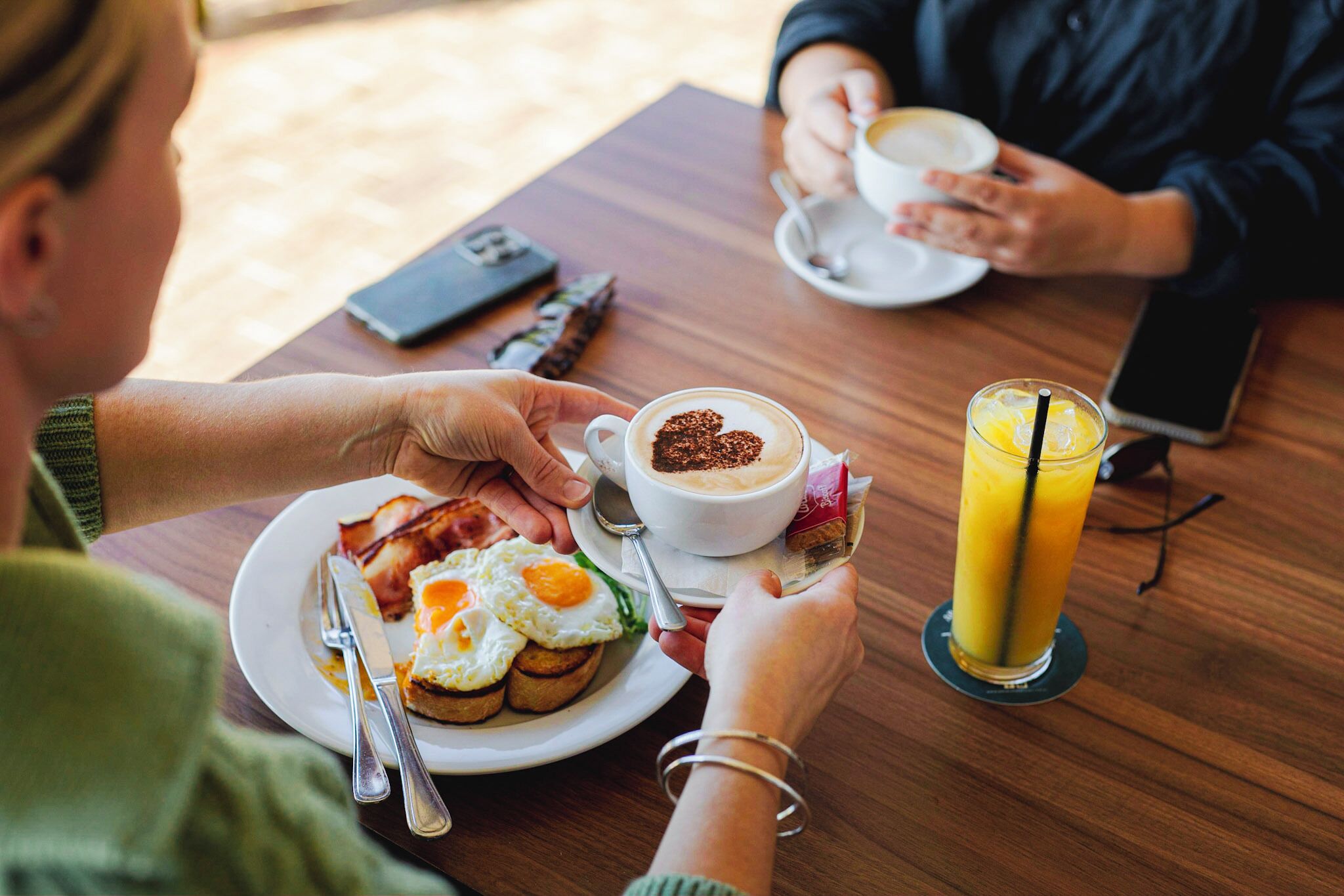 A wooden table with breakfast plates, a cup of coffee, and a glass of orange juice.