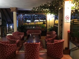 Un restaurante con sillas de estampado floral rojo y una mesa central, rodeado de luces de cuerda e instalaciones de plantas en macetas.