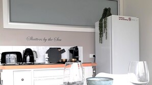 Una cocina con cafetera, tostadora y refrigerador. Hay dos copas de vino y un bol en la encimera.