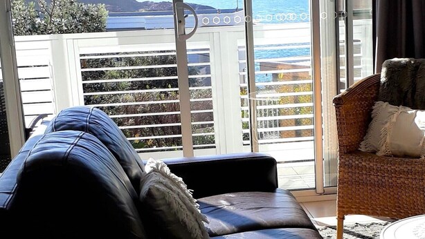Un balcón con vista al mar, un sofá y una silla de mimbre.