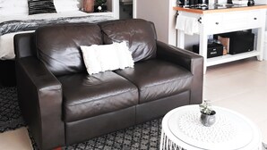 Una habitación de hotel moderna con un sofá de cuero, una cama con almohada a rayas, una mesita de noche con lámpara, una cafetera y un espejo grande.
