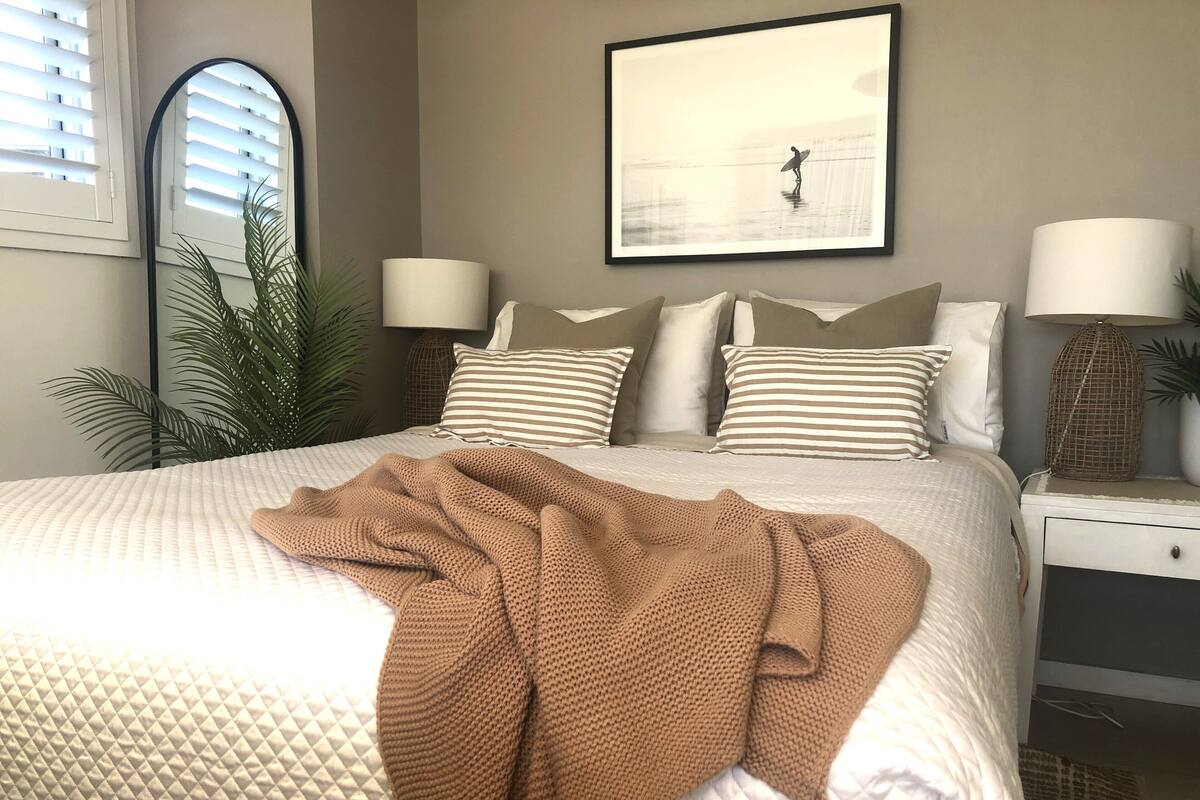 A neatly made bed with a brown blanket, striped pillows, and a framed picture on the wall.