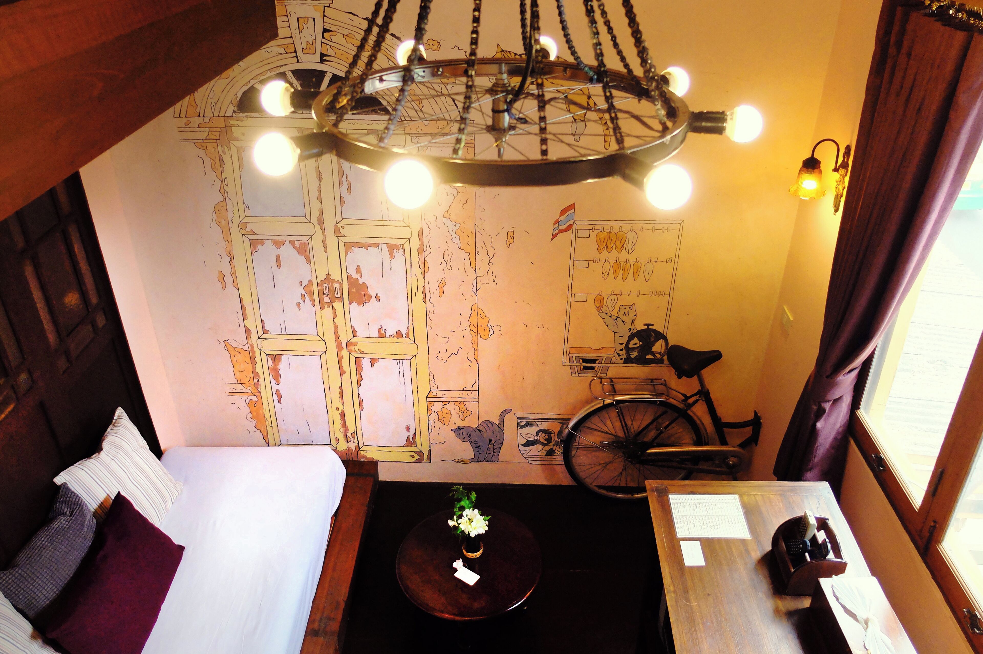 A room with a bed, a table with a vase, a bicycle, and a map on the wall.