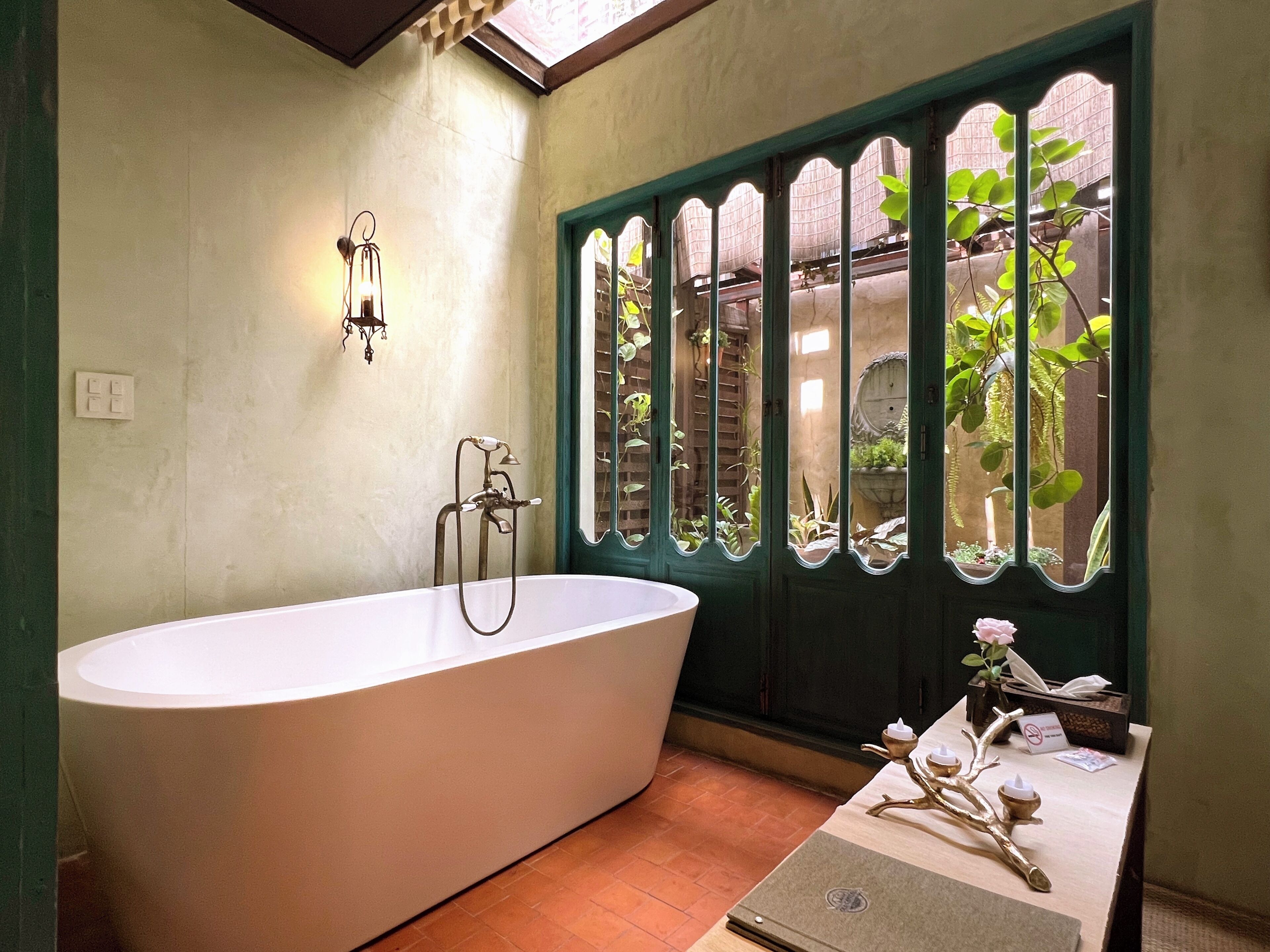 A bathroom with a freestanding bathtub, a wall-mounted light fixture, and a window with decorative glass panes.