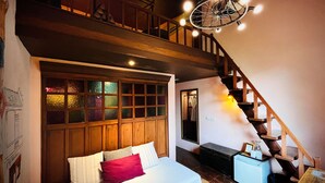 A bedroom with a wooden headboard, a bed with white and striped bedding, a small blue dresser, and a staircase with wooden railings. - Old Capital Bike Inn (Bangkok)