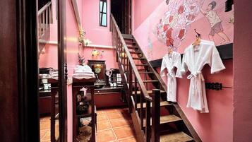 A pink-walled hallway with a staircase, a wooden railing, and a wall-mounted rack with white robes.