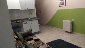 Une cuisine de taille réduite avec des meubles blancs, un évier et un radiateur. Le sol est recouvert d’un tapis à motifs et un des murs est peint en vert.