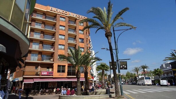 Un hôtel à plusieurs étages doté de balcons, de palmiers et surplombant un ciel d’un bleu limpide.