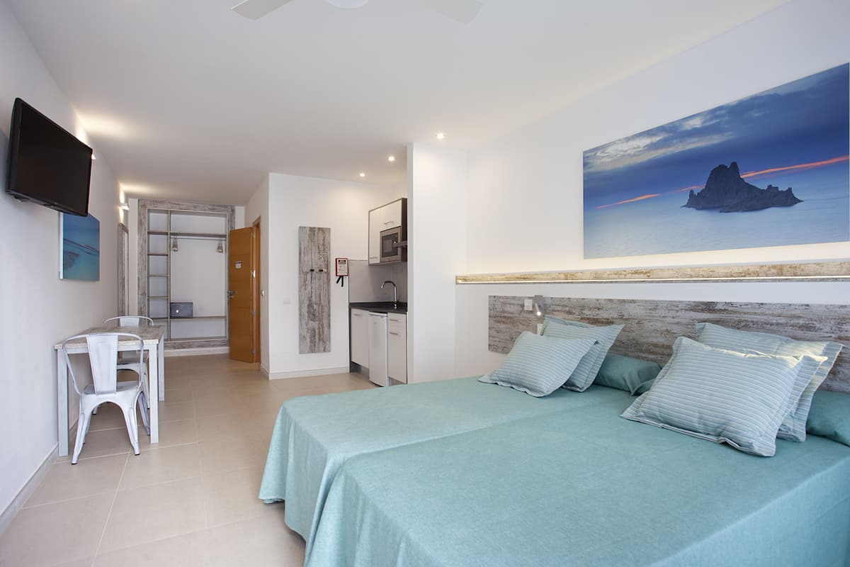 A bedroom with two beds, a desk, and a kitchenette.