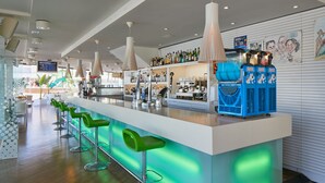 Zona de bar moderna con una barra alargada, taburetes verdes y una variedad de botellas y vasos en estanterías.