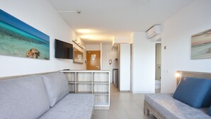 Una sala de estar moderna y bien iluminada, con un sofá, una cama pequeña y un televisor montado en la pared.