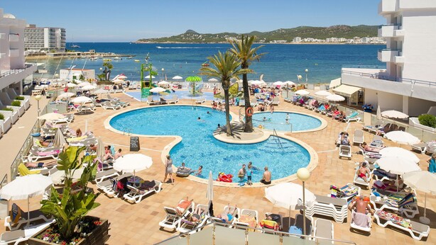 Un área de piscina en la azotea con varias piscinas, tumbonas, sombrillas y vistas al mar y edificios distantes.