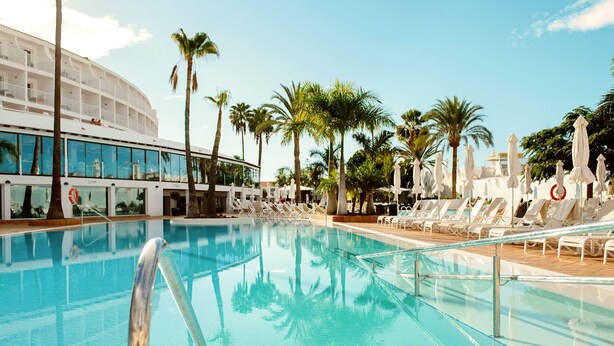 A swimming pool with lounge chairs and palm trees. - Sunprime Atlantic View Suite & Spa (San Bartolomé de Tirajana)