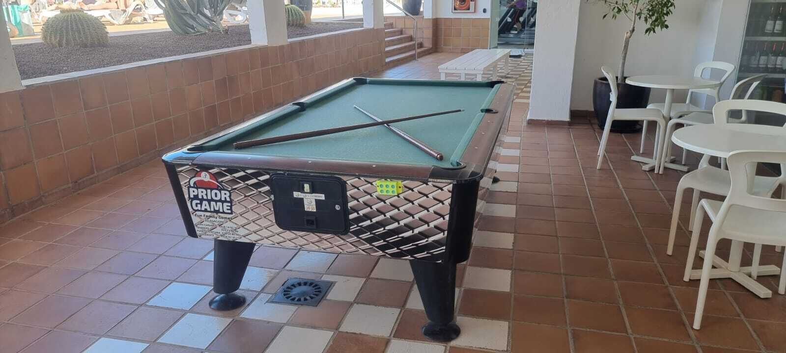 A pool table with a 'PRIOR GAME' label, surrounded by white plastic chairs and a tiled floor.