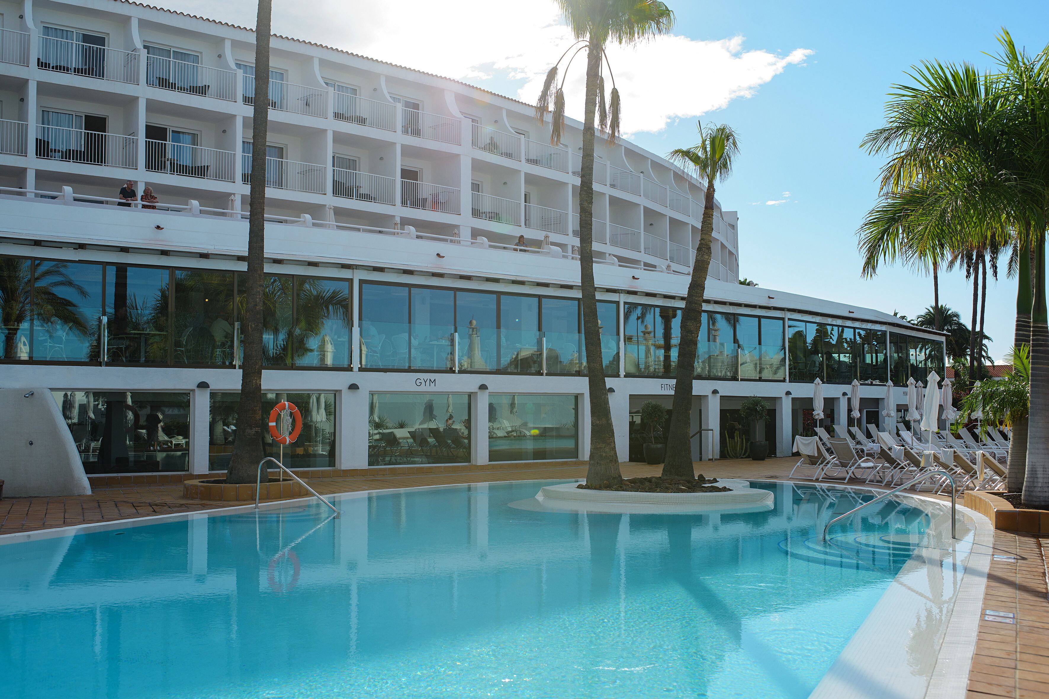 A hotel with a swimming pool, multiple balconies, and sun loungers.
